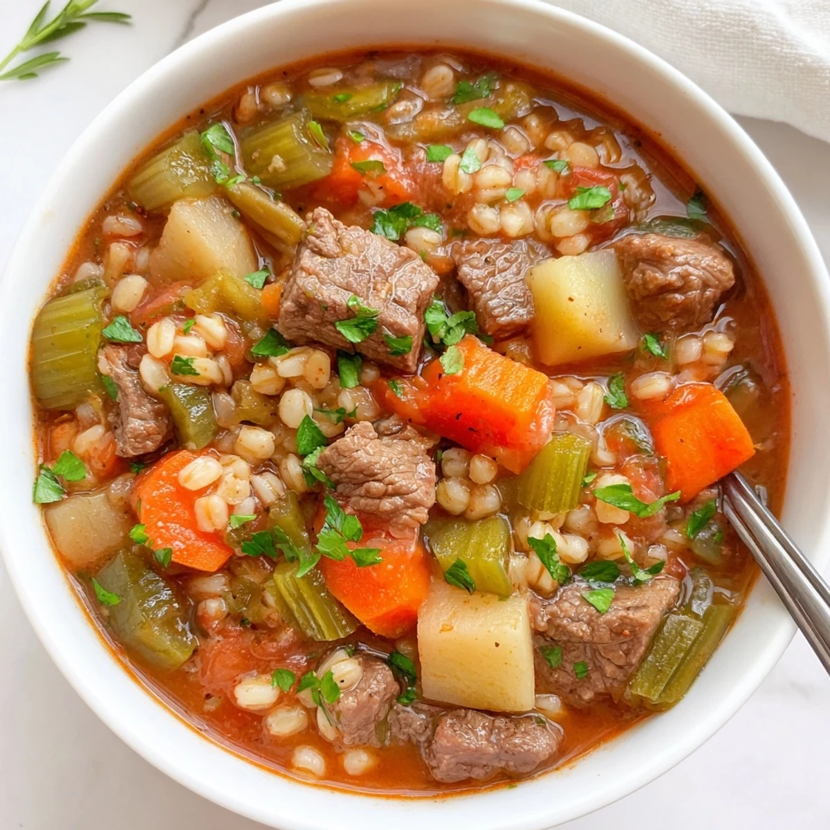 Close-up of Hearty Beef and Vegetable Barley Stew in a Dutch oven, featuring seared beef, carrots, celery, and pearl barley simmering in a rich tomato-based broth.