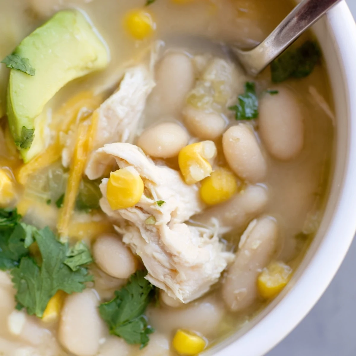A spoon dips into the hearty chili, revealing tender chicken and beans beneath.