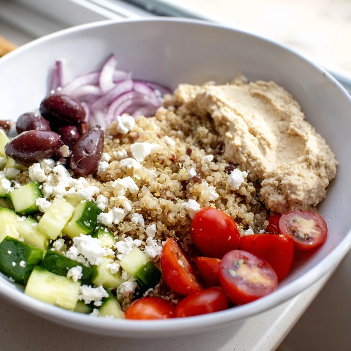 A close-up of the Mediterranean Quinoa Bowl topped with creamy hummus, cherry tomatoes, and crumbled feta over fluffy quinoa and greens.  