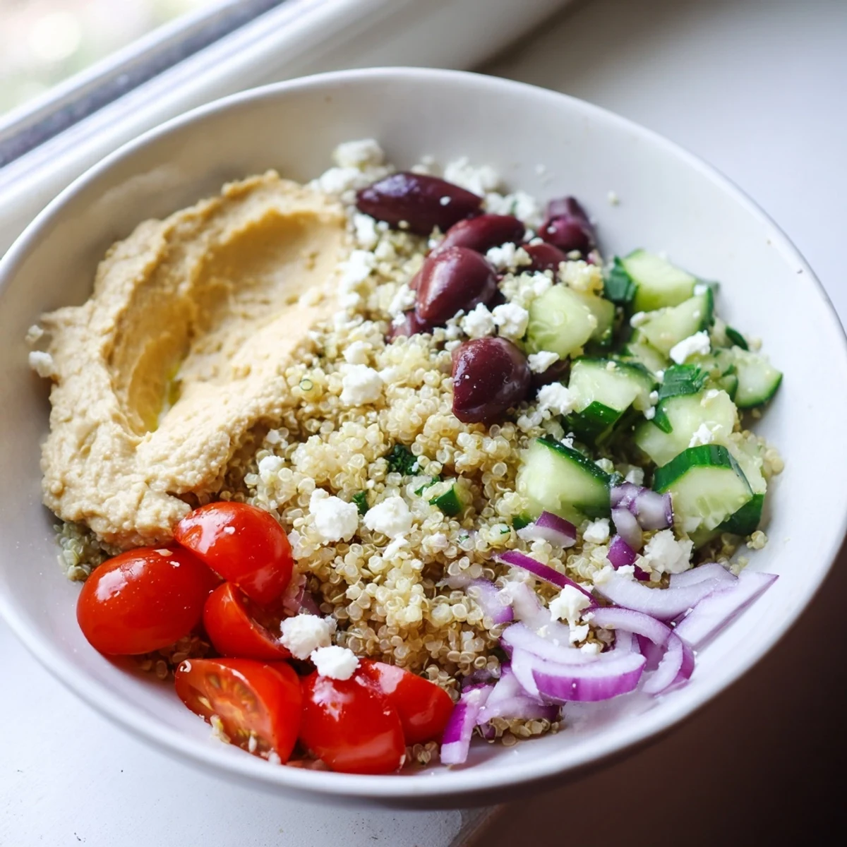 Colorful Mediterranean Quinoa Bowl served in a white bowl, featuring spinach, red onion, and a generous scoop of hummus.