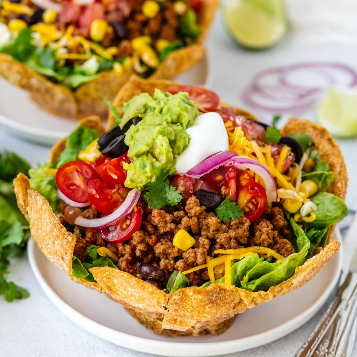 Golden brown, crunchy homemade tortilla bowls hold a vibrant taco salad filled with seasoned ground beef, black beans, corn, and cheddar cheese.