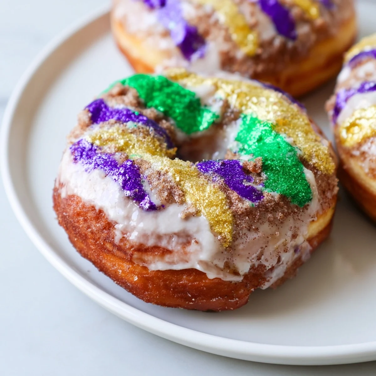 Close-up of Mardi Gras King Cake Donuts with a lemon glaze, showcasing the stuffed cinnamon sugar swirl filling and New Orleans colors.