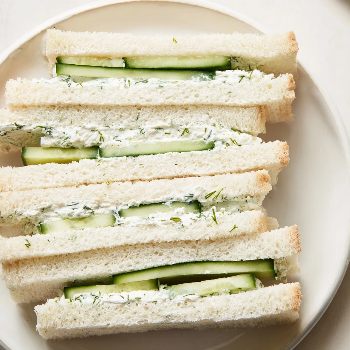 Lightly chilled cucumber sandwiches with cream cheese, garnished with fresh dill and chives, ready to serve.