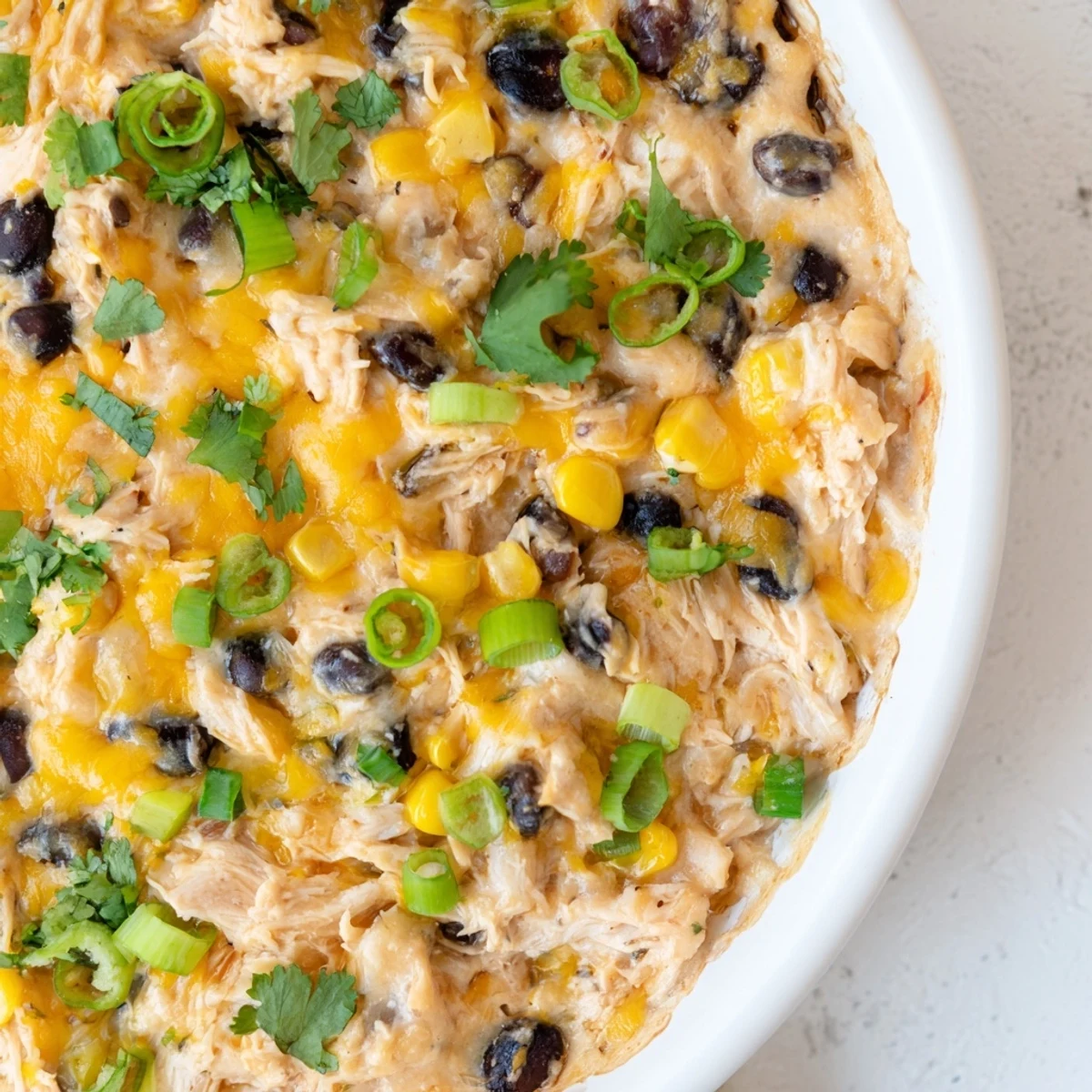 Golden, bubbly Chicken Enchilada Dip with cheese and cilantro garnish in a white baking dish, served with tortilla chips.