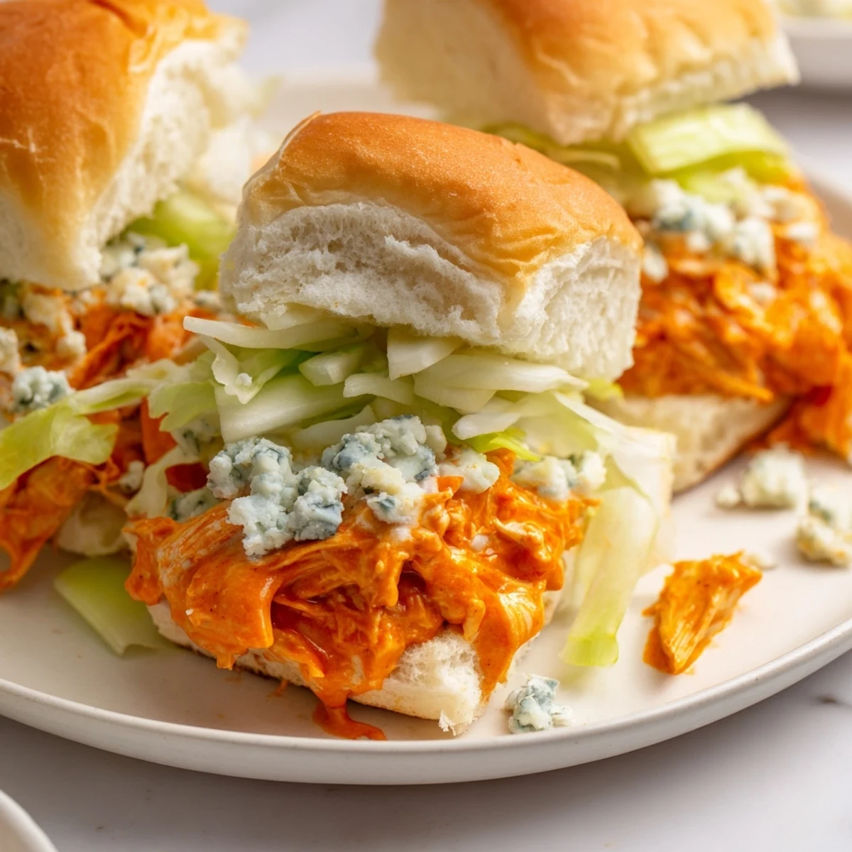 A close-up view of buffalo chicken sliders with blue cheese crumbles and vibrant lettuce on a rustic wooden board.