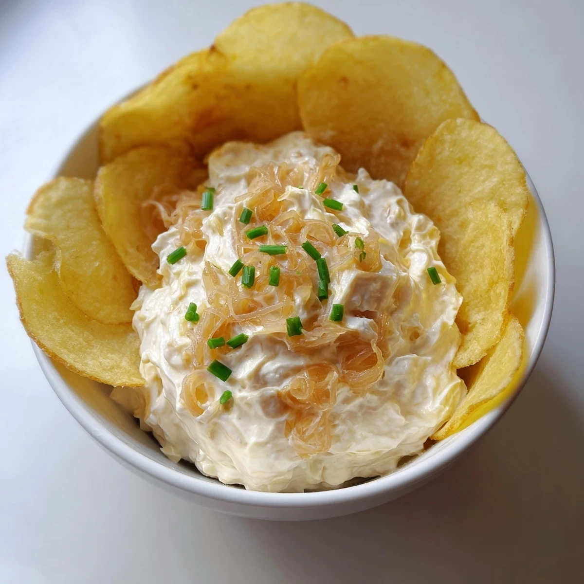 Rich, cheesy onion dip with a spoonful taken, paired with crunchy potato chips on a rustic serving platter.