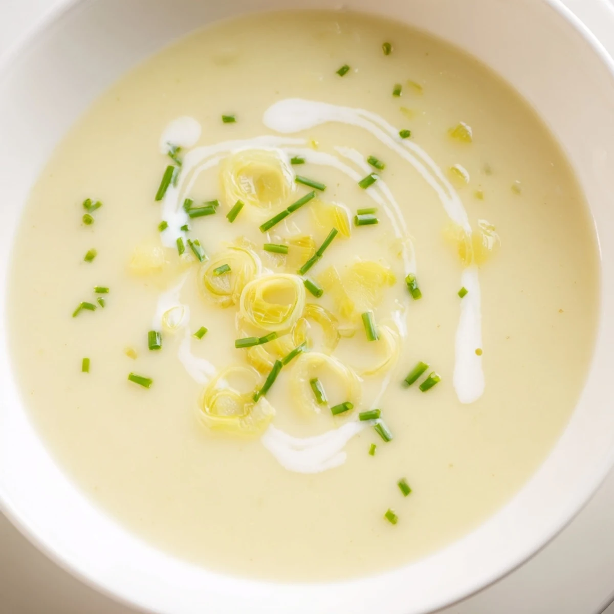 Close-up of velvety Leek and Potato Soup with Cream, steam rising from rich, pureed vegetables in a cozy white ceramic bowl.