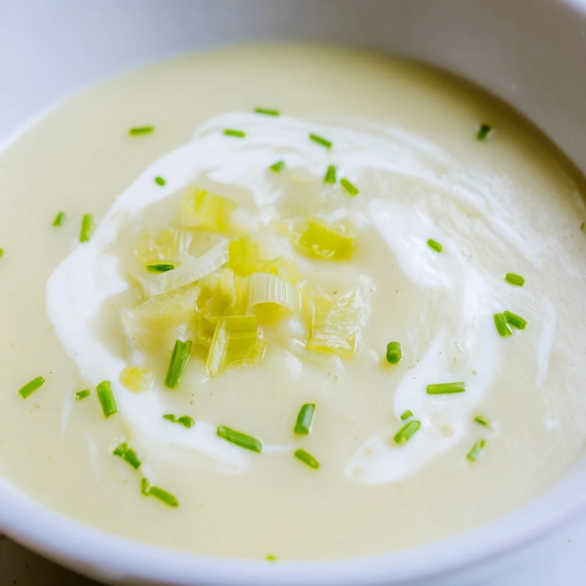 Silky smooth Leek and Potato Soup in a white ceramic bowl, topped with a swirl of cream and chopped parsley.