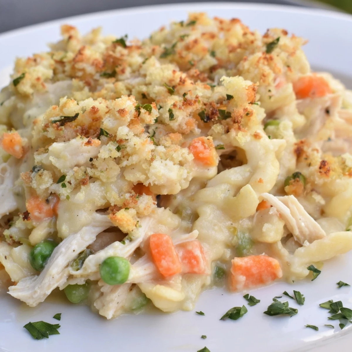 A close-up of Chicken Noodle Casserole with Crumble, golden topping glistening beside a fresh garden salad.