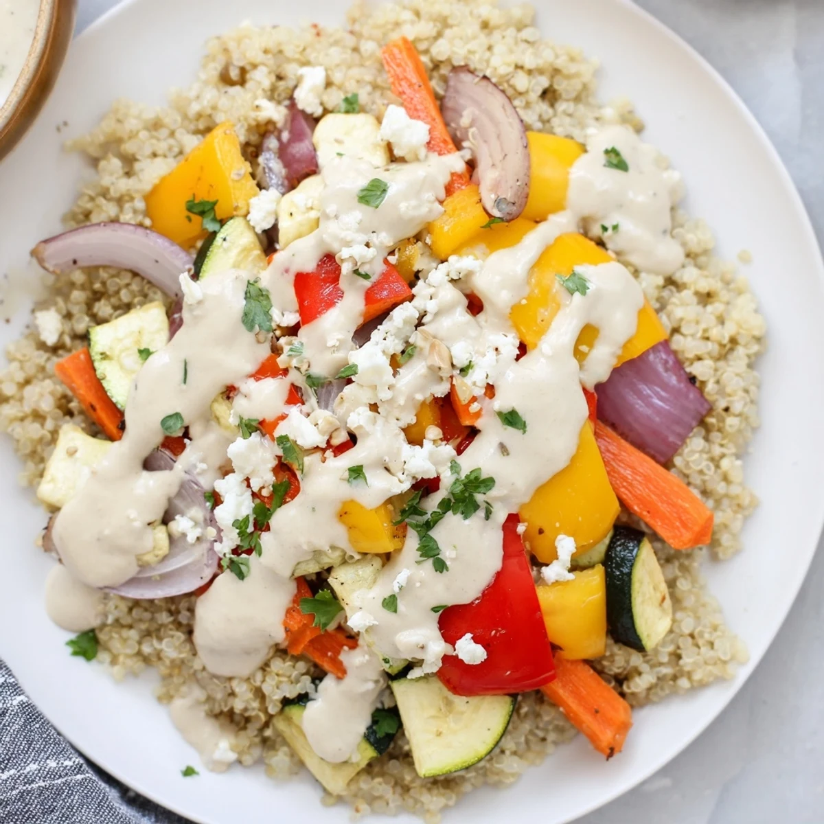 Healthy roasted vegetable quinoa bowl with colorful seasonal produce, finished with toasted pumpkin seeds and a zesty lemon-tahini dressing on a wooden table.