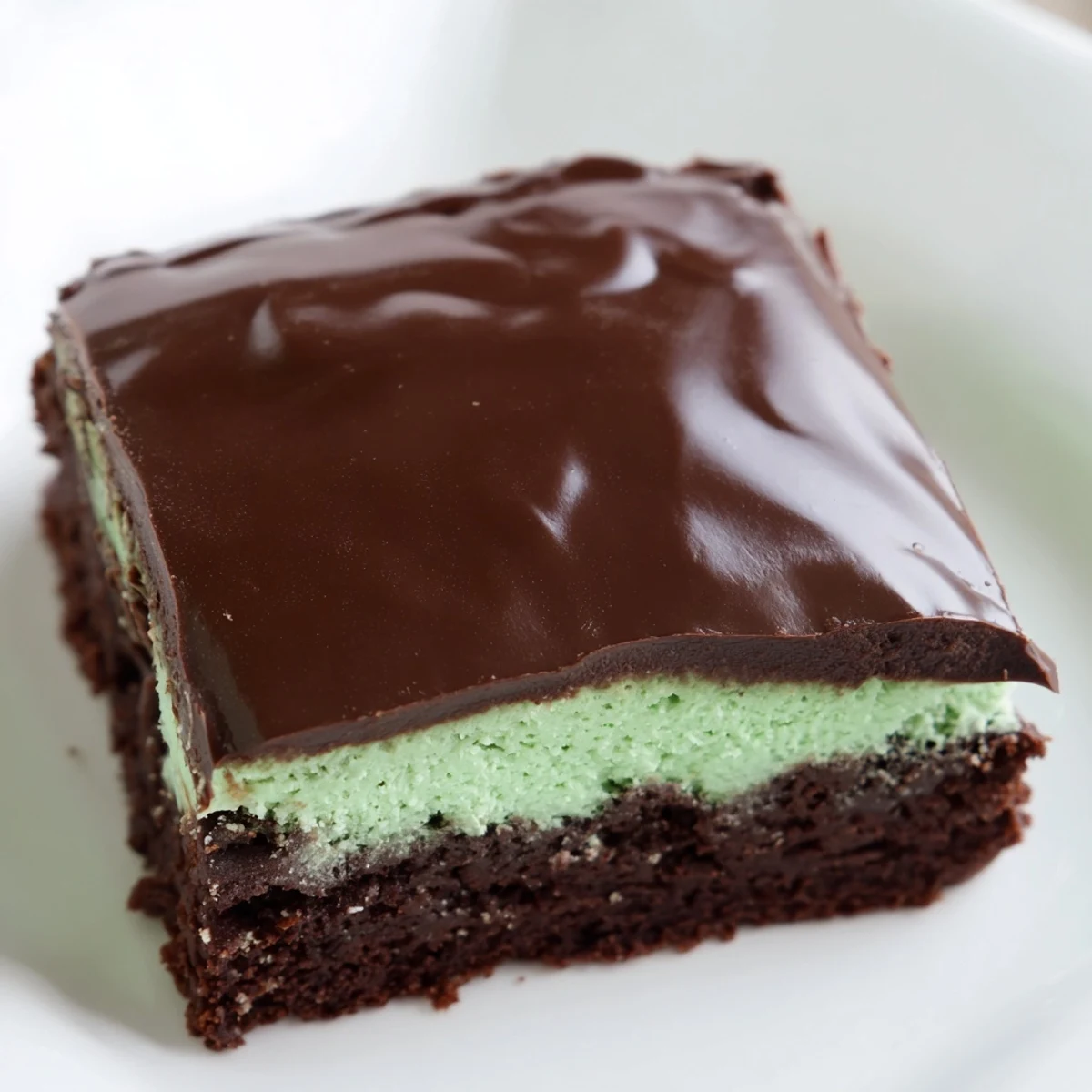 Decadent Green Mint Brownies sliced into squares, showing layers of fudgy chocolate, pale green mint cream, and shiny ganache.