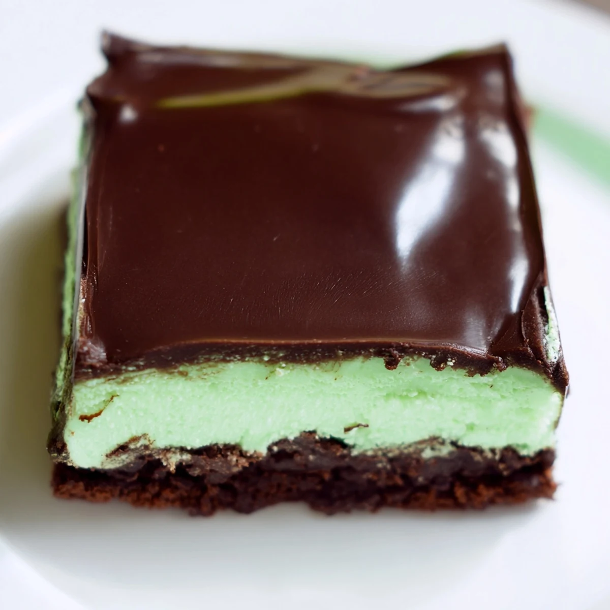 Freshly glazed Green Mint Brownies on a white plate, with a glass of cold milk and visible peppermint speckles.