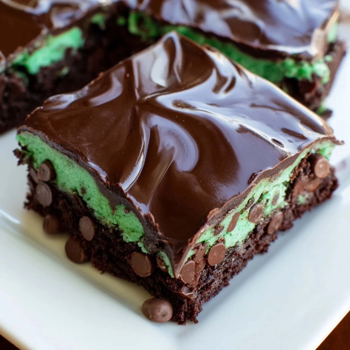 Freshly cut Green Mint Brownies with Chocolate Chips arranged on a cooling rack, with a glass of milk in the background.