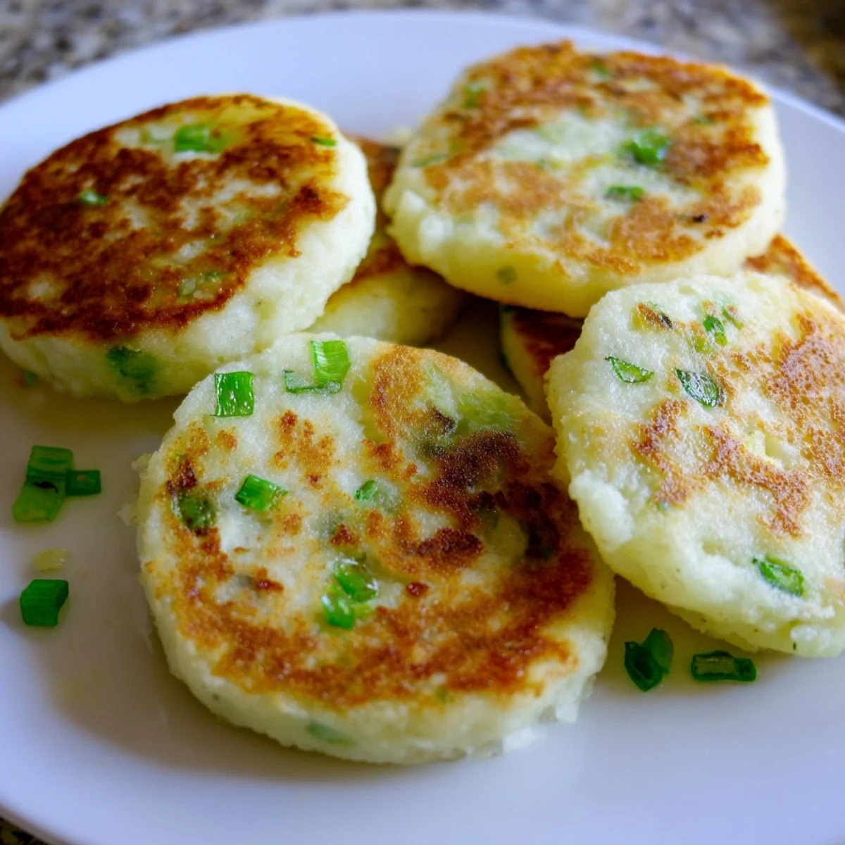 Golden, pan-fried Irish Potato Cakes with Scallions sit on a rustic plate, ready to serve with butter.
