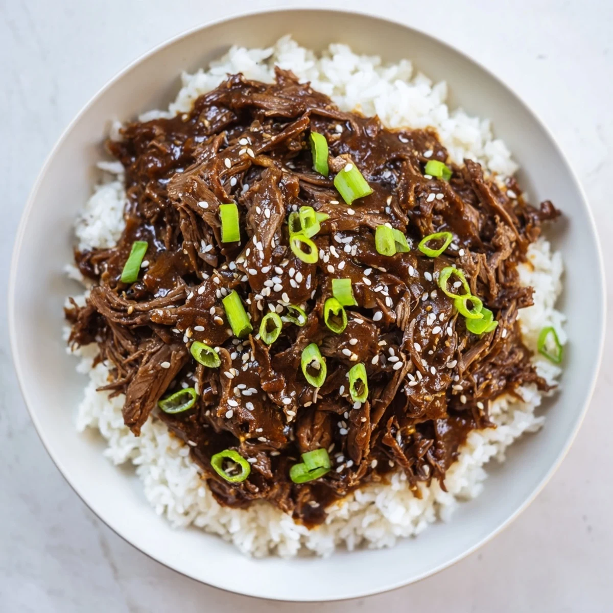 Tender shredded Slow Cooker Korean Beef piled high in a bowl with fluffy white rice, garnished with green onions and sesame seeds.