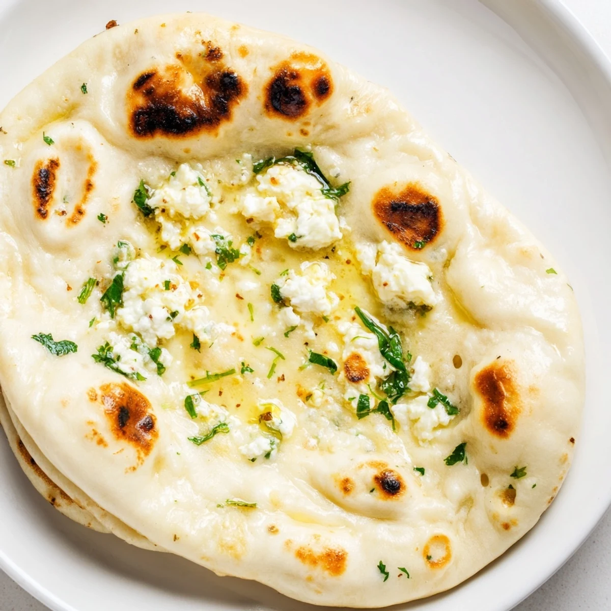 Freshly cooked Cottage Cheese Garlic Naan with visible garlic bits and green cilantro on a rustic wooden board.