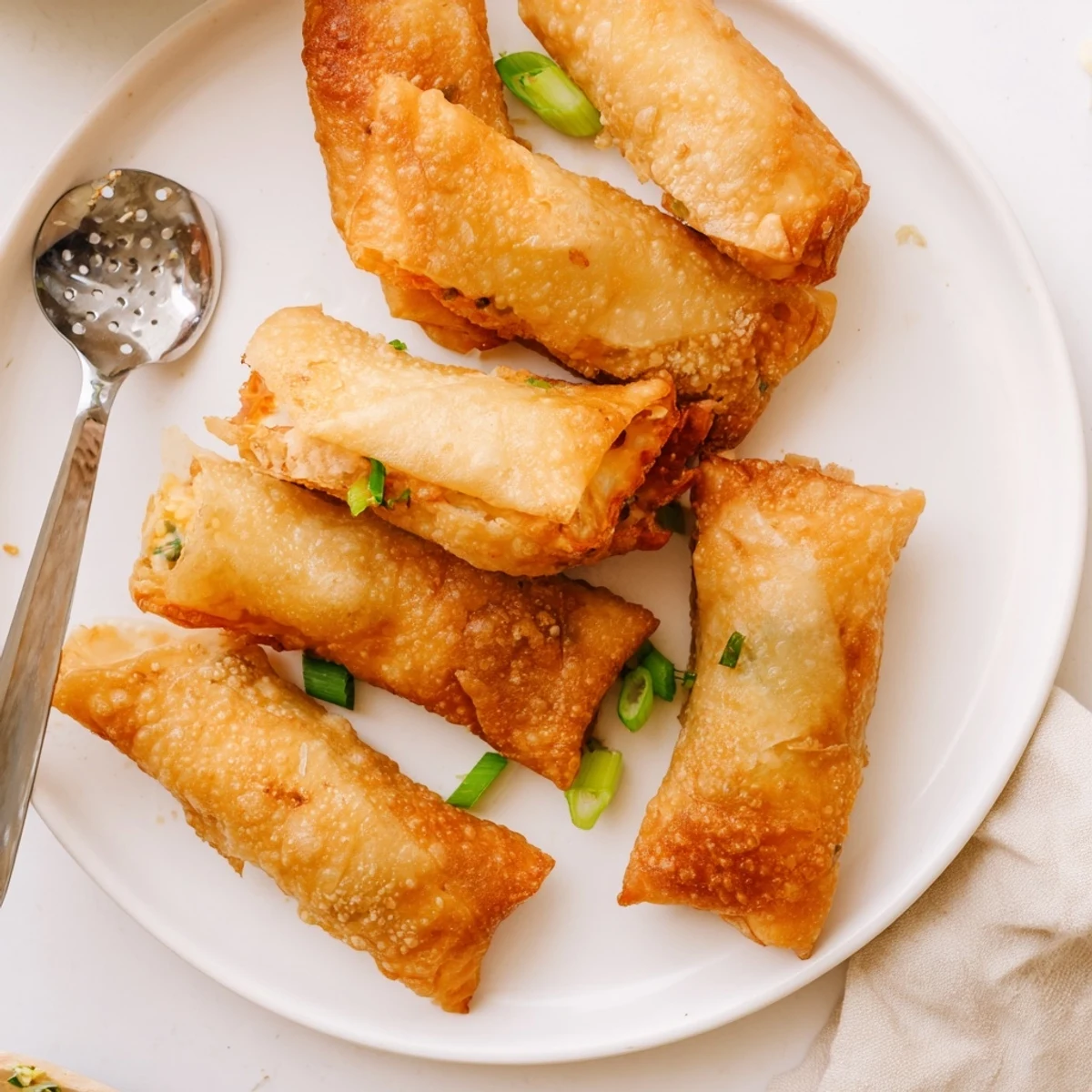 A hand holding a Mini Jalapeño Popper Egg Roll, revealing melted cheese and jalapeños with a side of dipping sauce.