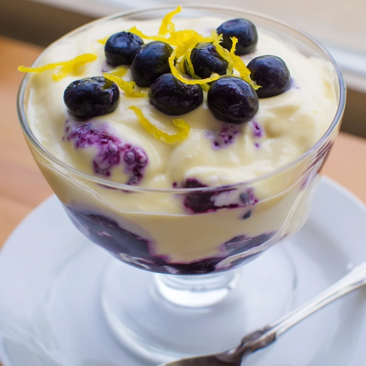 A close-up view of Lemon Blueberry Mousse in a glass, featuring layers of vibrant purple compote and creamy yellow lemon mousse topped with fresh berries.
