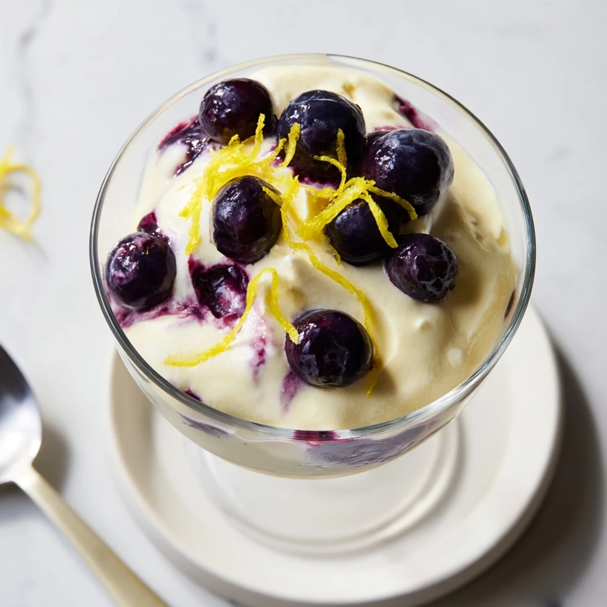 An elegant serving of Lemon Blueberry Mousse in a tall glass, garnished with a twist of lemon zest and a sprig of fresh mint leaves.