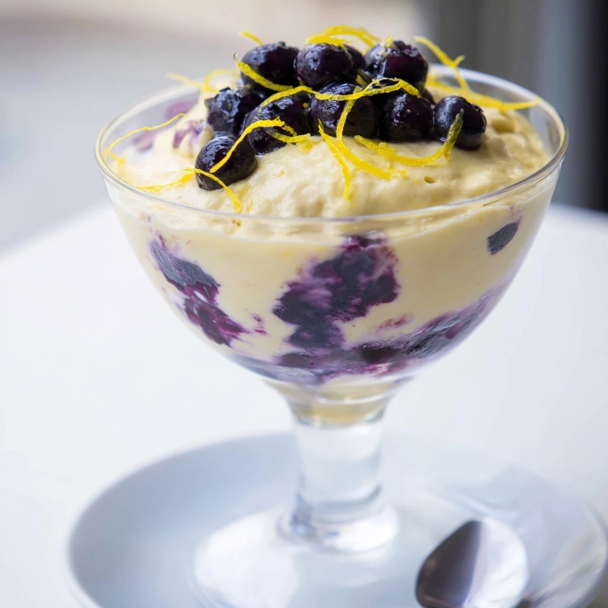 This airy Lemon Blueberry Mousse dessert is displayed in a glass, revealing smooth layers of tangy citrus and sweet blueberry flavors.