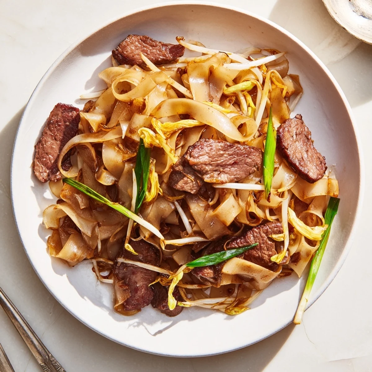 A close-up of classic Beef Chow Fun highlighting glossy noodles, seared beef, and crisp vegetables in a pan.