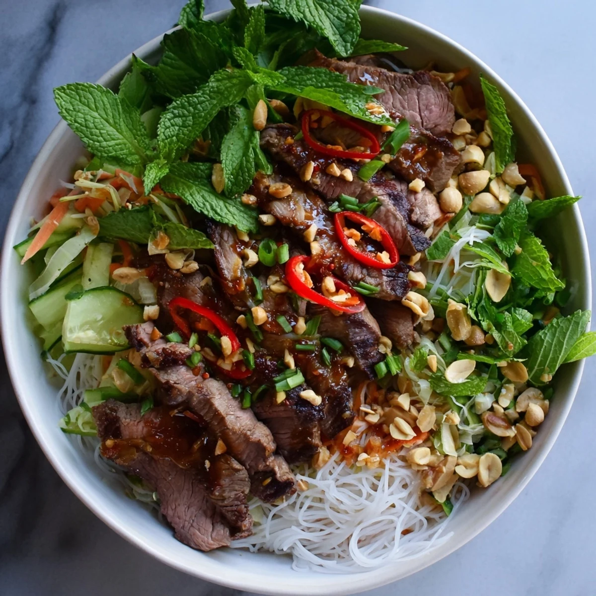 A close-up of Bun Bo Xao, sautéed beef slices over rice noodles with fresh mint and crunchy peanuts.