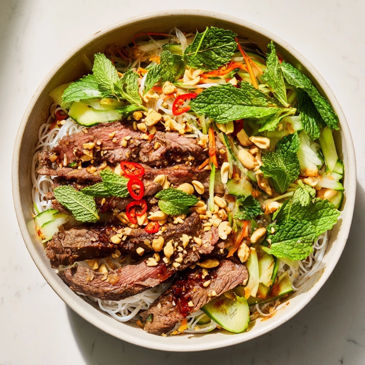 In a bright bowl, Bun Bo Xao features stir-fried beef, julienned carrots, cucumber, and a drizzle of nuoc cham.