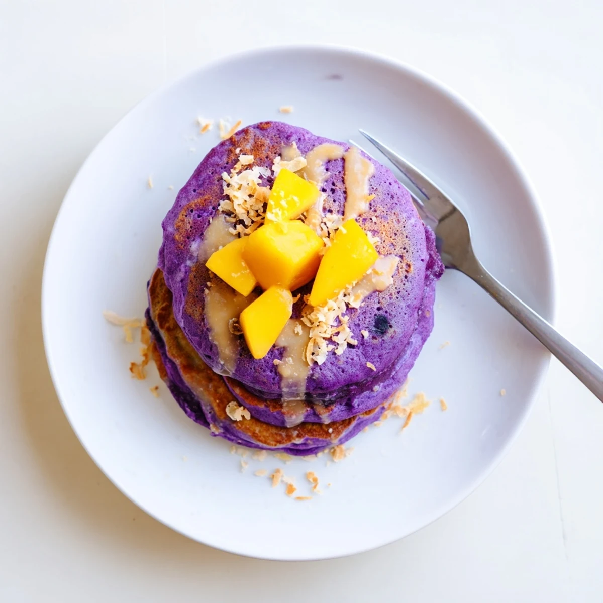 Golden-brown Ube Mochi Pancakes served warm with fresh mango slices and toasted coconut flakes on a rustic plate.
