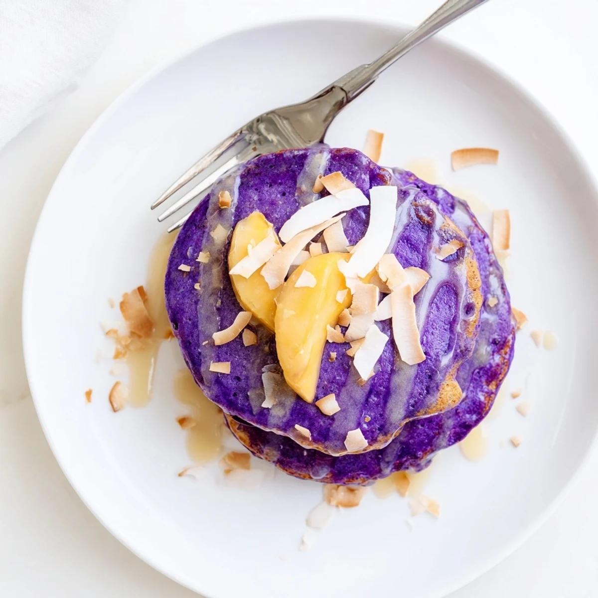 Vibrant purple Ube Mochi Pancakes with a chewy texture, ready to be enjoyed with maple syrup and fresh berries.