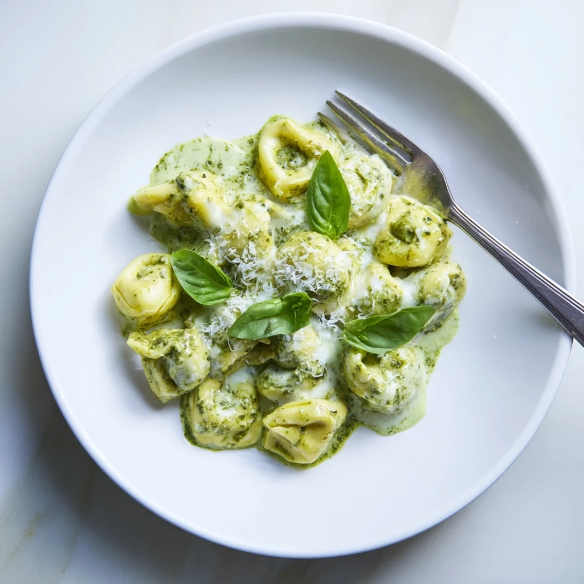 Creamy Pesto Alfredo Tortellini twirls on a white plate, garnished with fresh basil and pine nuts for a weeknight dinner.