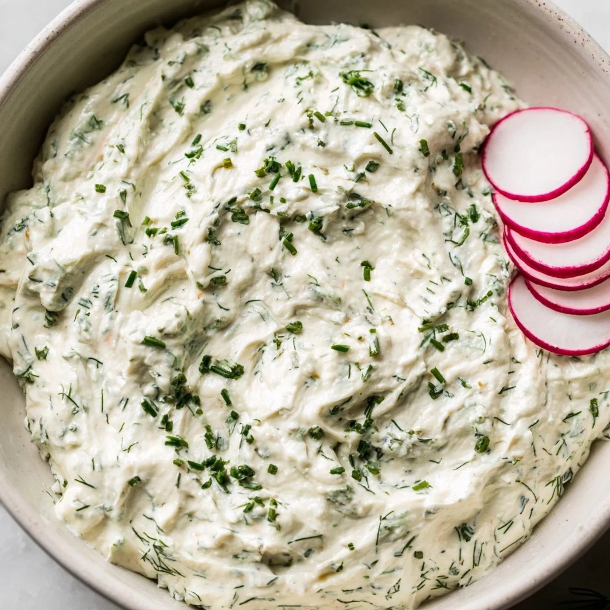 The Simple Easter Herb Cheese Dip in a rustic bowl surrounded by radish slices and crisp crackers for dipping.