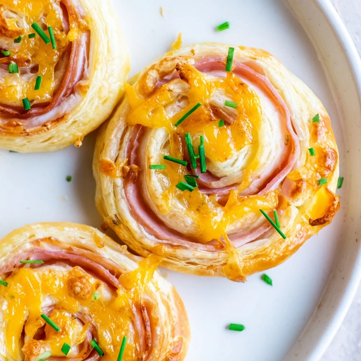 Freshly baked Easter Ham Cheddar Pinwheels reveal flaky pastry layers, melted sharp cheddar, and savory ham slices on a rustic board.