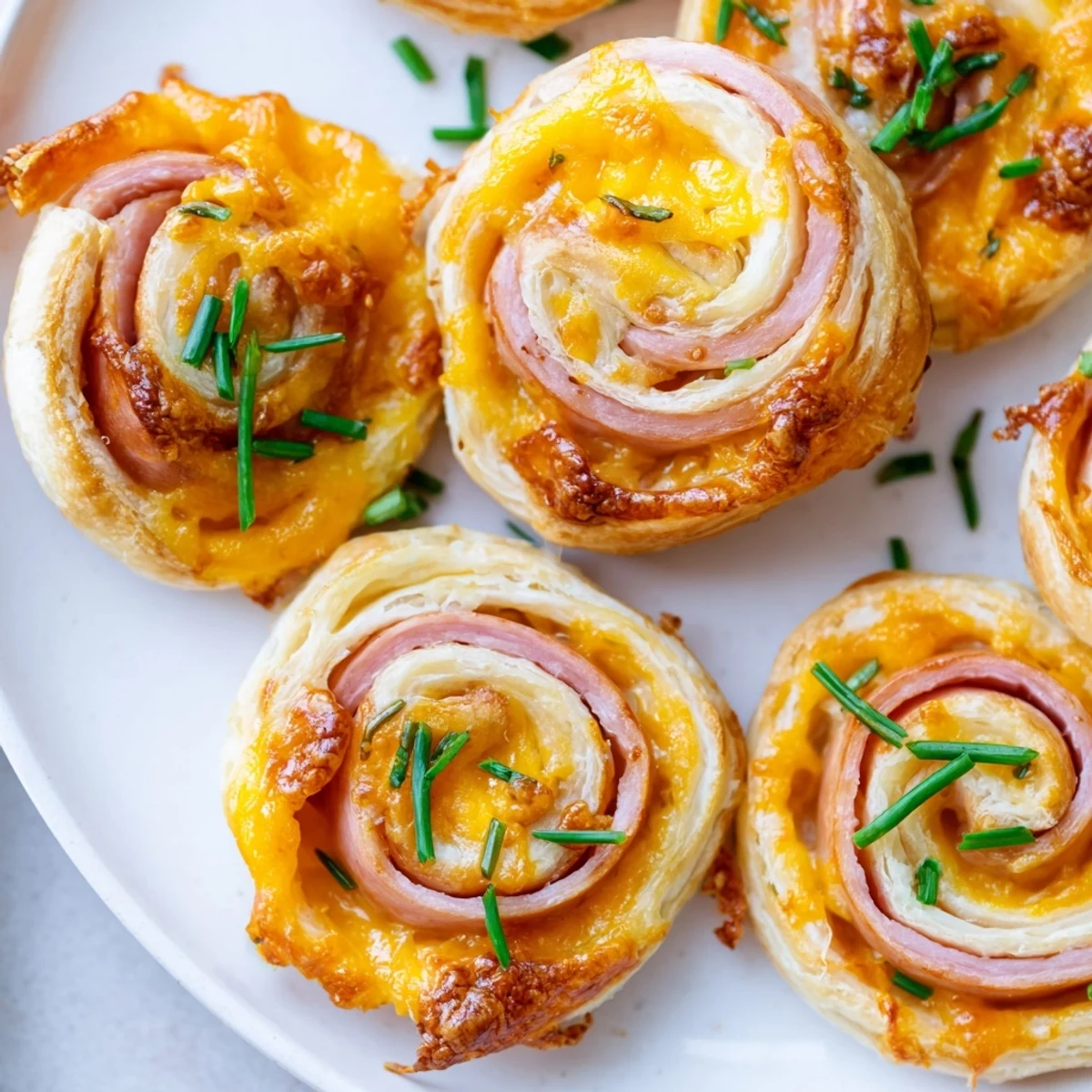A close-up of Easter Ham Cheddar Pinwheels shows golden, puffed pastry with herbs, perfect for spring appetizer spreads.