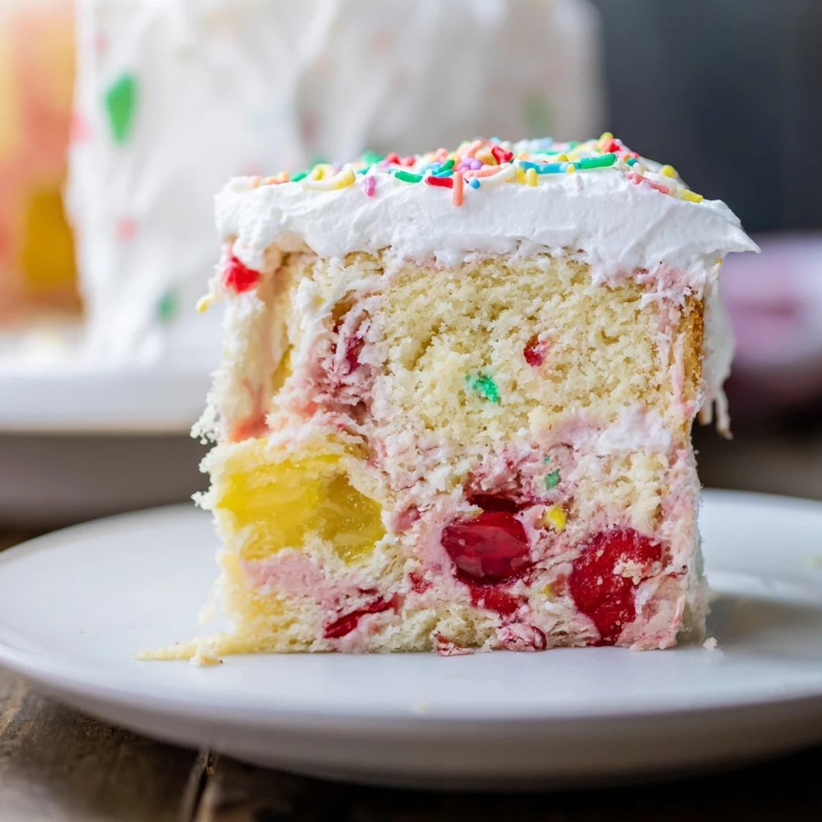 A slice of Easter Poke Cake with Vanilla Gelatin and Fruity Topping, featuring vibrant pink and yellow gelatin soaking into a moist vanilla base.