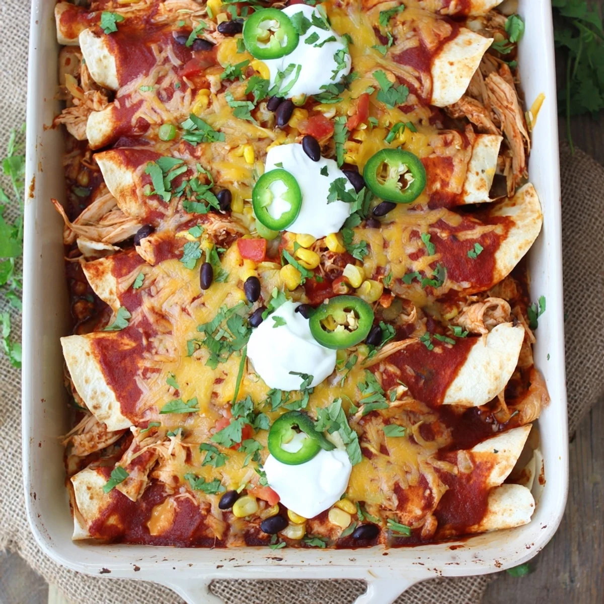 Sizzling Chicken Enchiladas in a baking dish, smothered in red sauce and garnished with jalapeños.