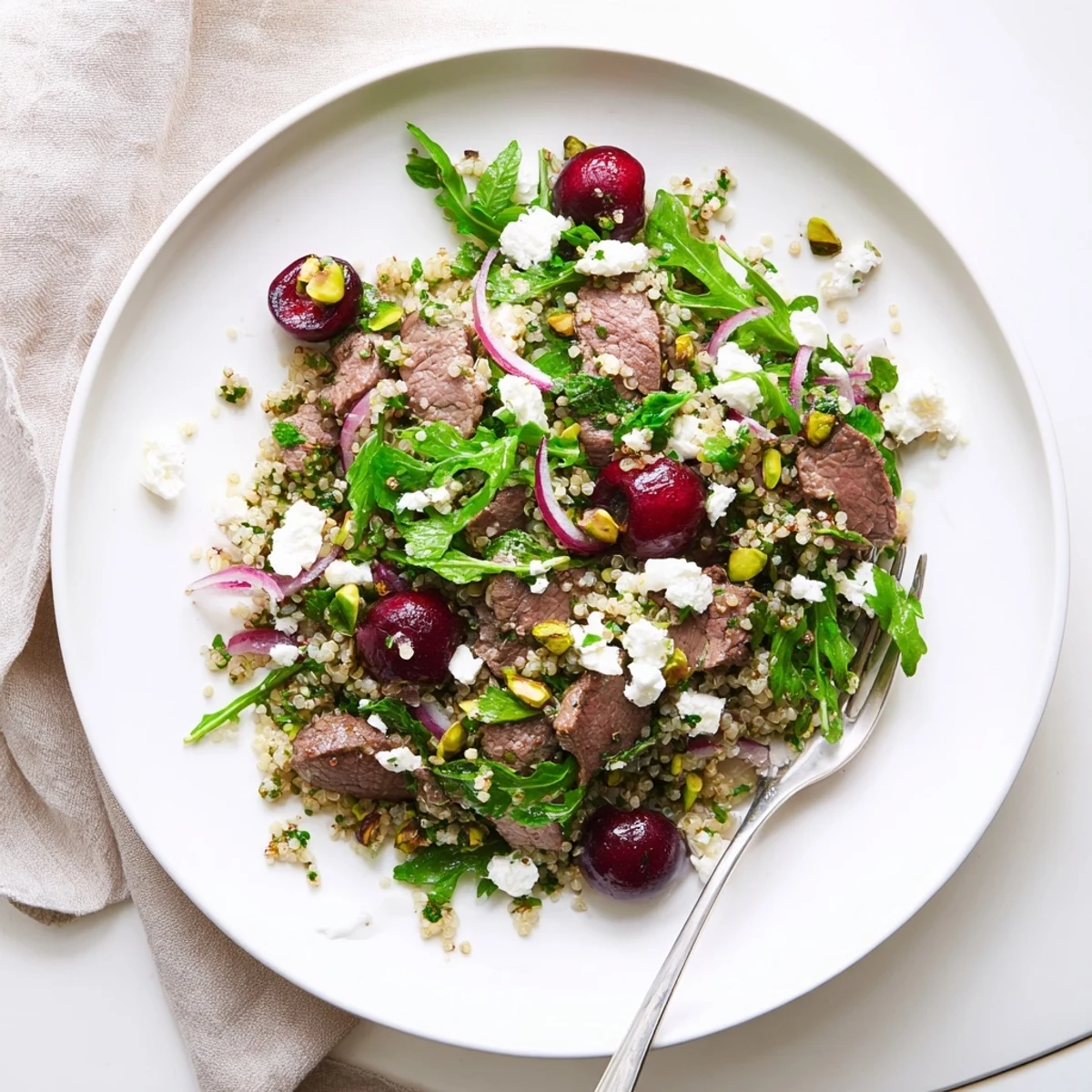 Colorful bowl of cherry quinoa salad with grilled lamb, baby spinach, red onion, and zesty dressing