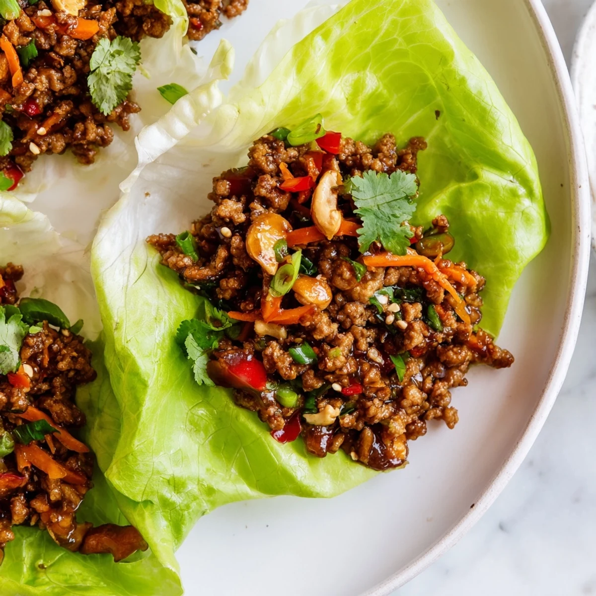 Golden brown seasoned beef with diced vegetables and chopped cashews nestled inside cool crisp lettuce leaves for easy handheld appetizers