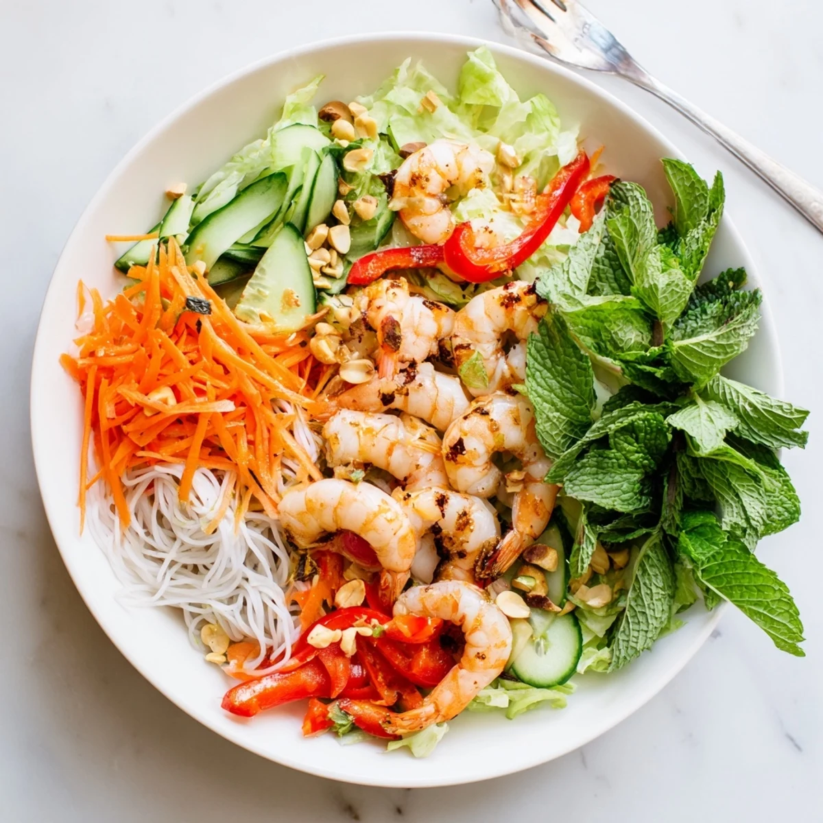 Colorful bowl of spring roll salad with spicy ginger dressing topped with shrimp and roasted peanuts
