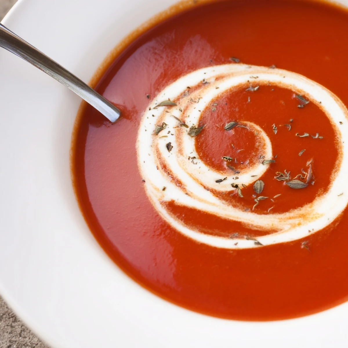 Velvety cozy tomato soup with roasted tomato chunks and drizzled cream on rustic wooden table