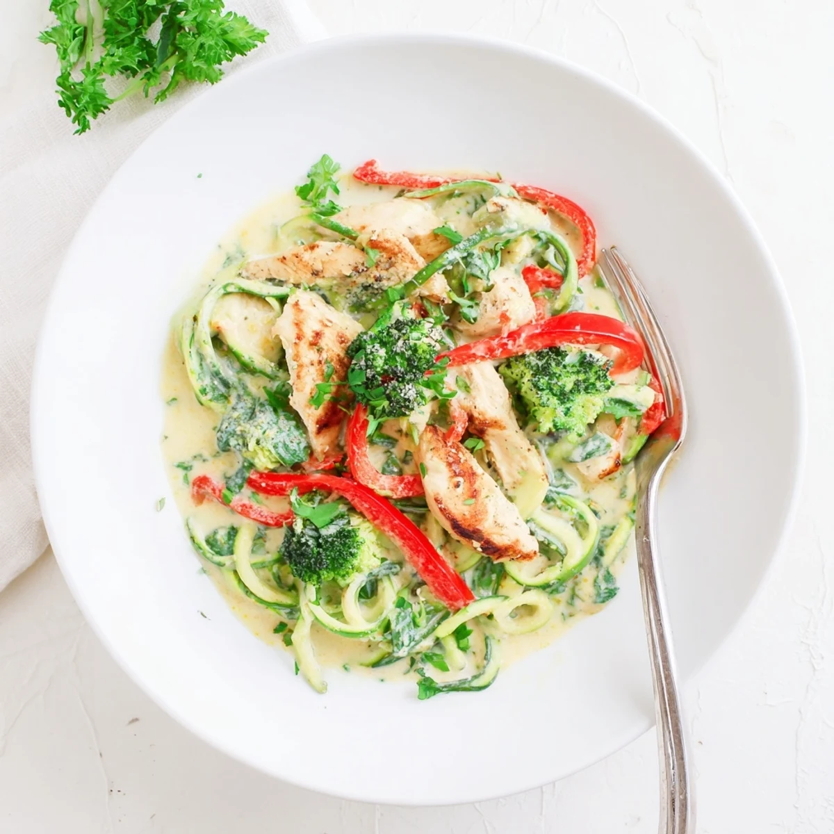 Vibrant low carb Alfredo featuring zucchini noodles, broccoli, bell peppers, and juicy chicken strips.