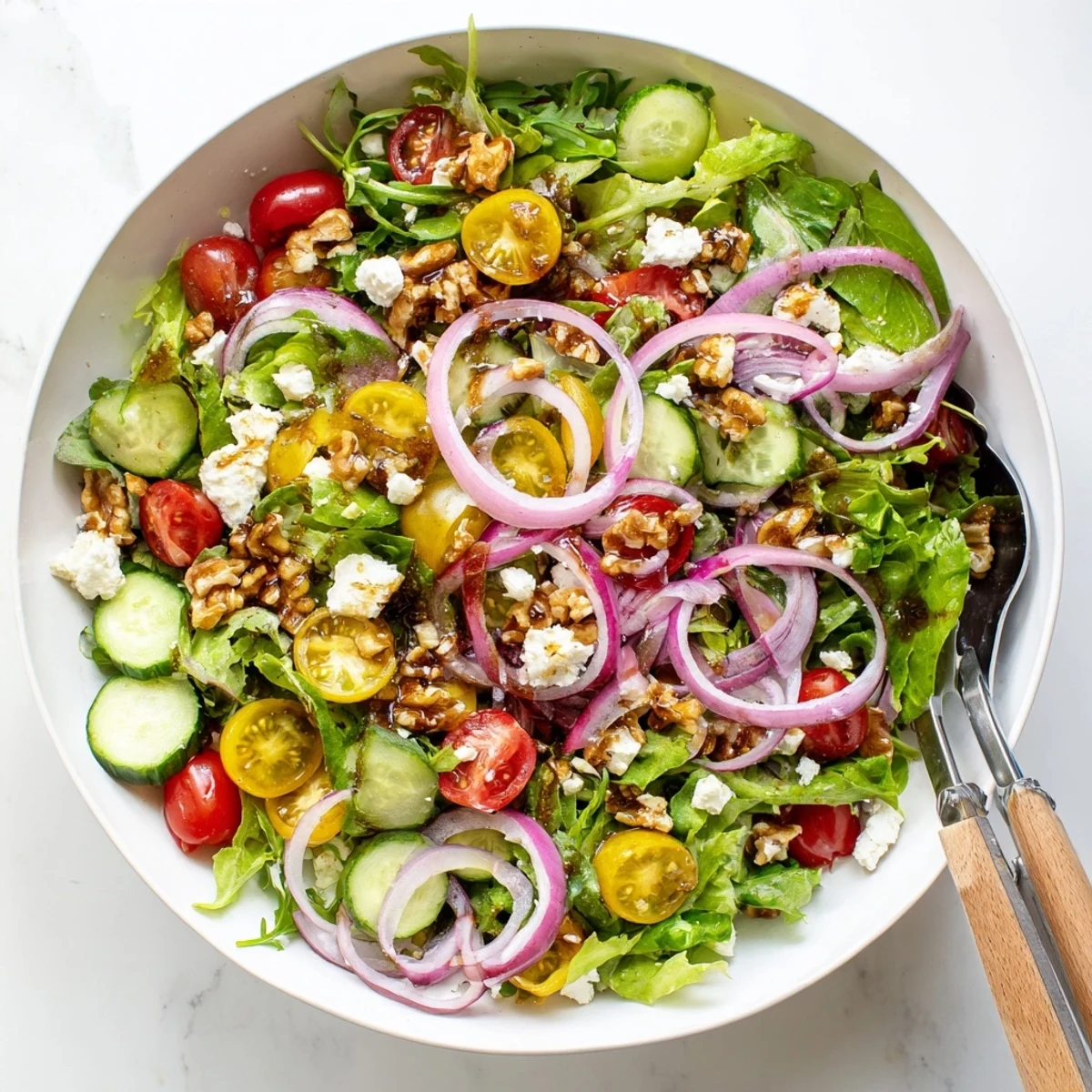 Fresh spring mix salad with balsamic honey dressing featuring crisp vegetables and crumbled feta in a white bowl.