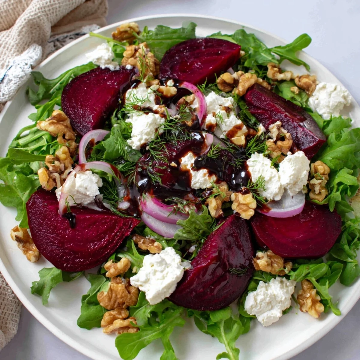 Colorful plate of roasted beet salad topped with creamy goat cheese, crunchy walnuts, and red onion