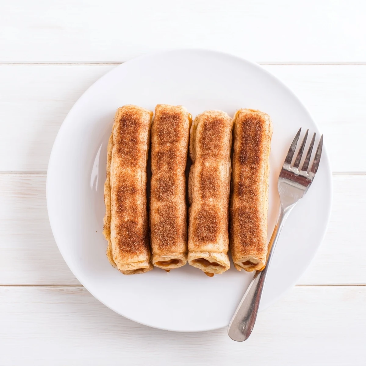 Golden brown dulce de leche pastries sprinkled with cinnamon sugar on a white plate