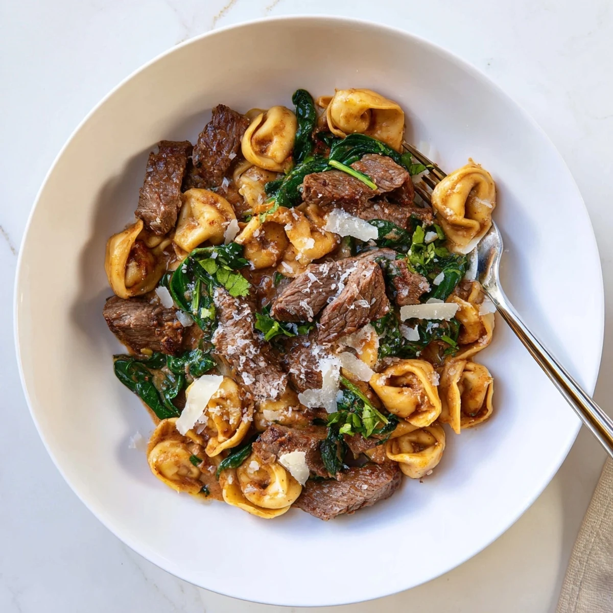 Plated garlic steak tortellini with wilted spinach and grated parmesan topping