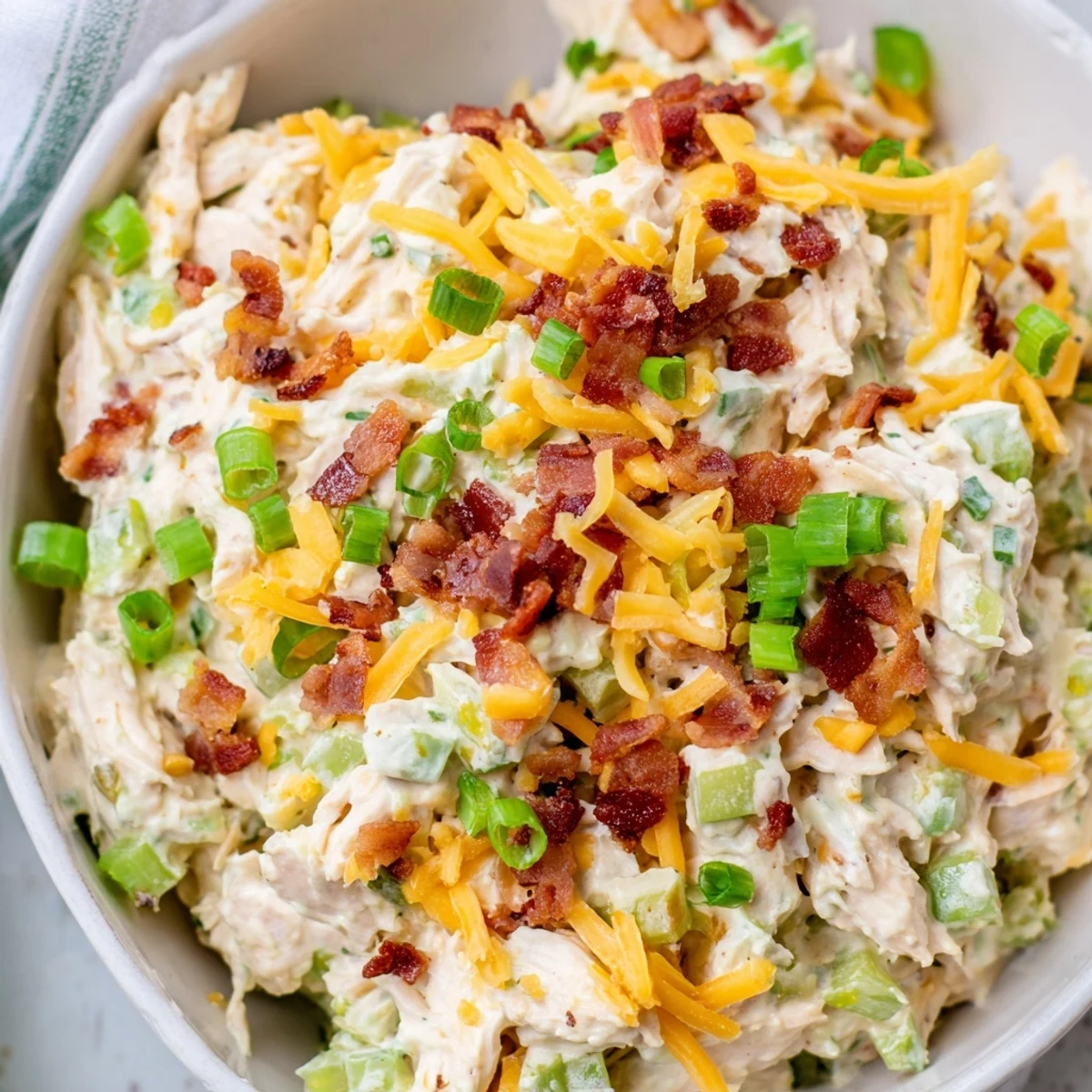 Keto-friendly chicken salad in white bowl topped with chopped celery and vibrant green jalapeno pieces