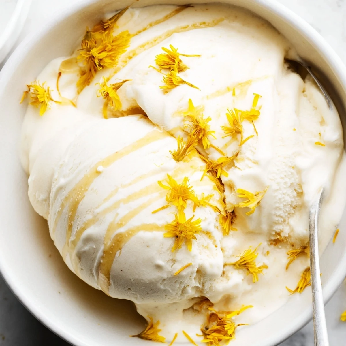 Creamy dandelion honey ice cream scoop topped with golden petals in a chilled bowl