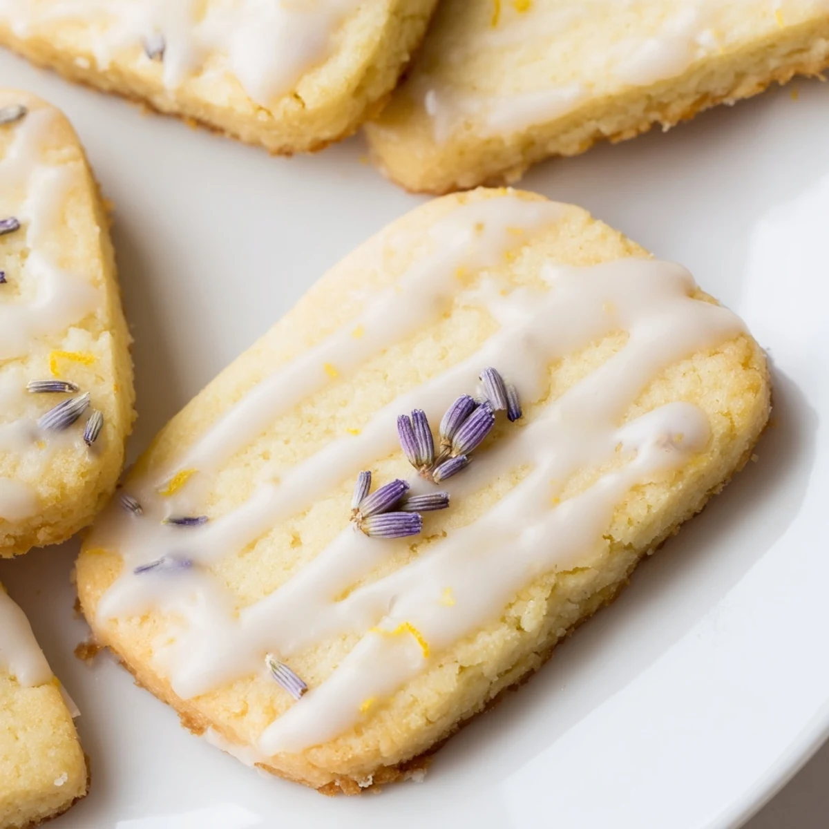 Iced Lemon Lavender Shortbread Cookies drizzled with bright citrus glaze on a rustic white serving plate