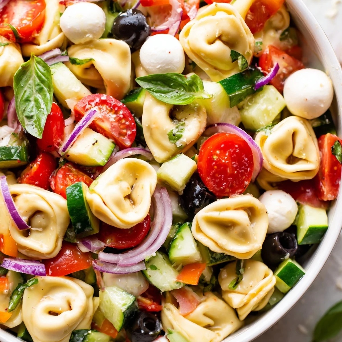 Cheese tortellini salad garnished with fresh basil, mozzarella balls, and crisp vegetables ready to serve