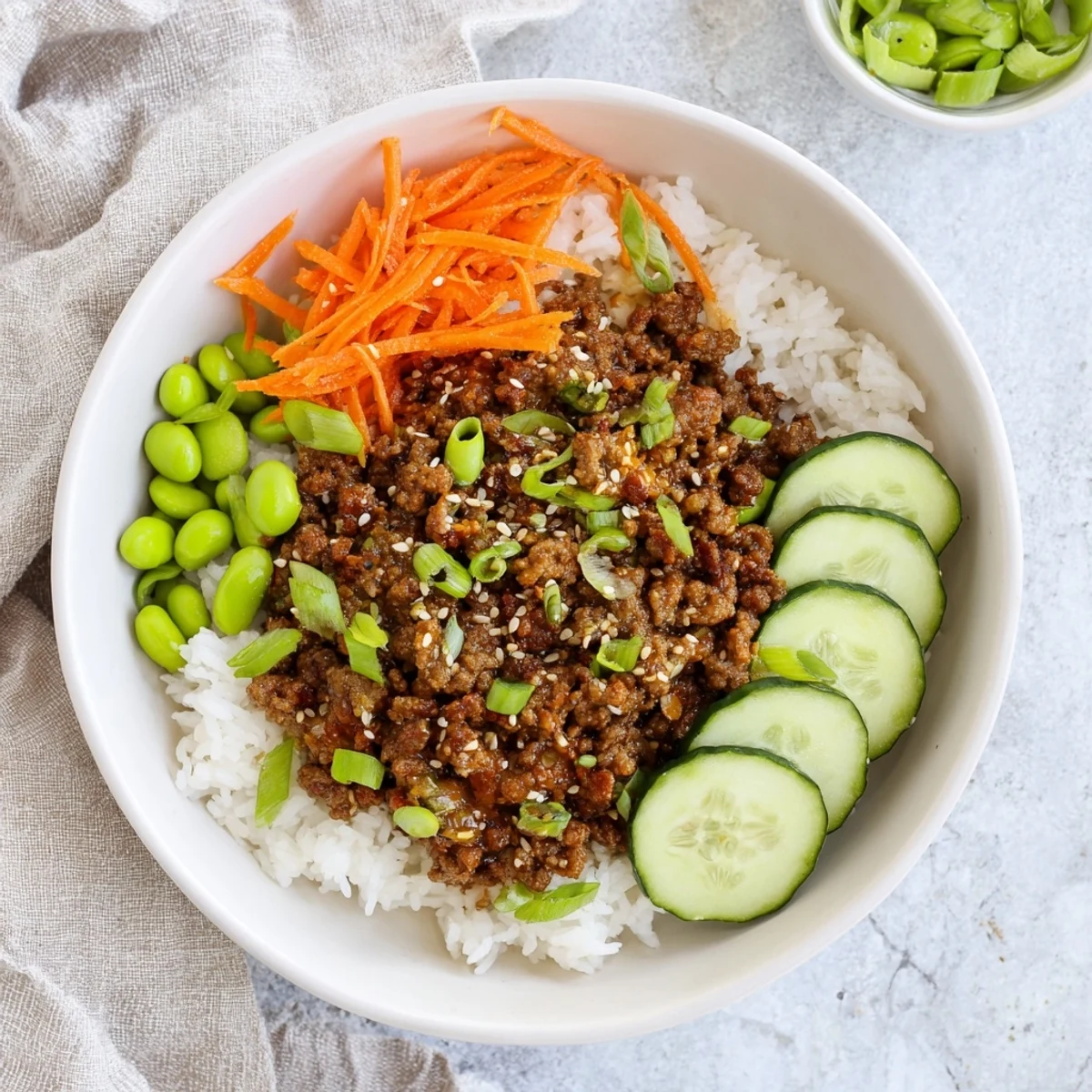 Steaming rice bowl topped with hot honey glazed beef, fresh cucumbers, carrots, and crunchy edamame