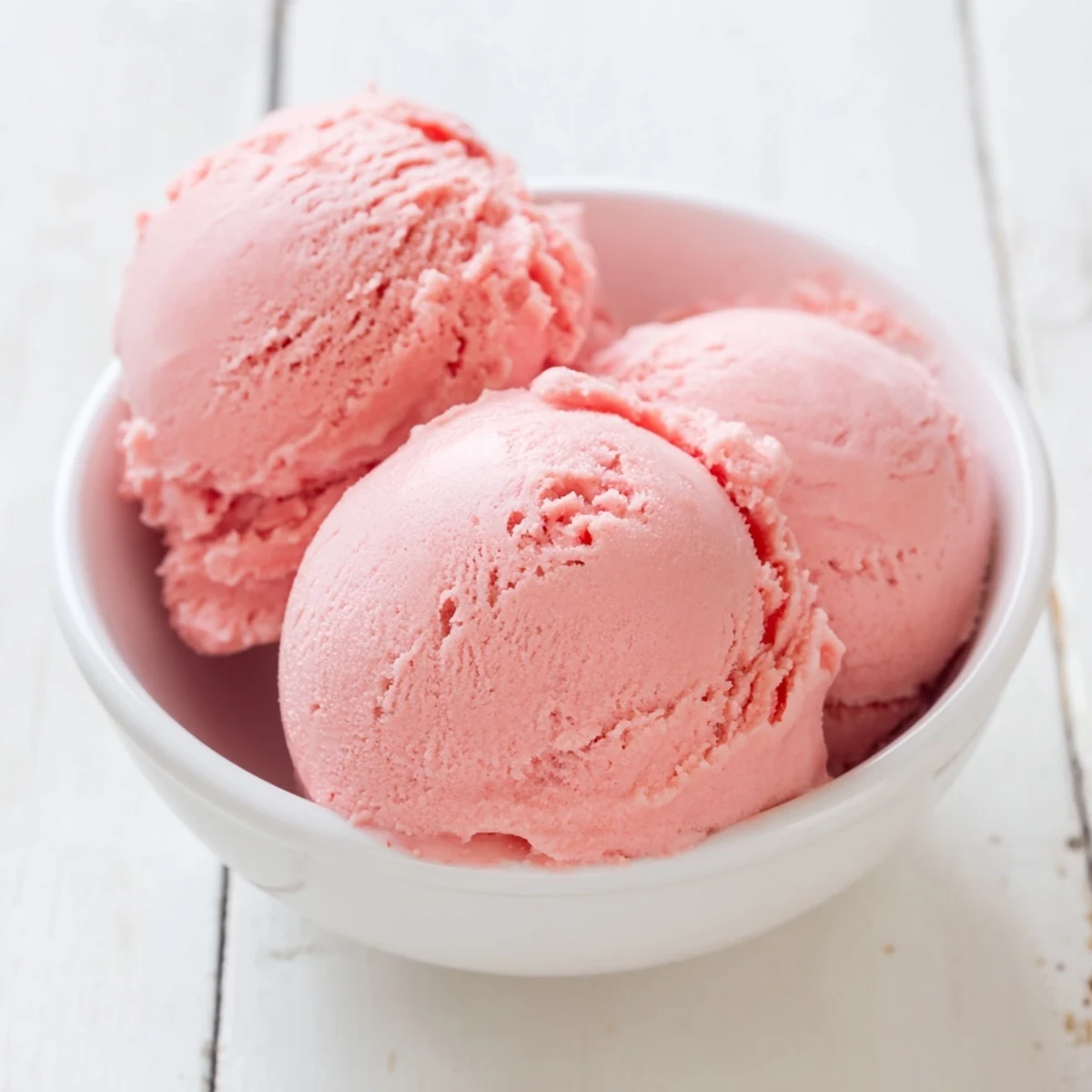 Pink scoops of homemade watermelon ice cream in a glass bowl garnished with fresh mint